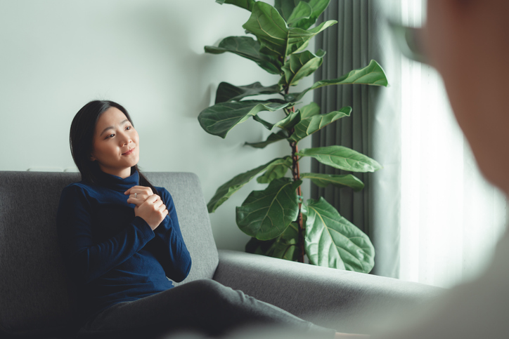 Asian woman sitting on sofa in counseling office and talking about problems to psychologist.