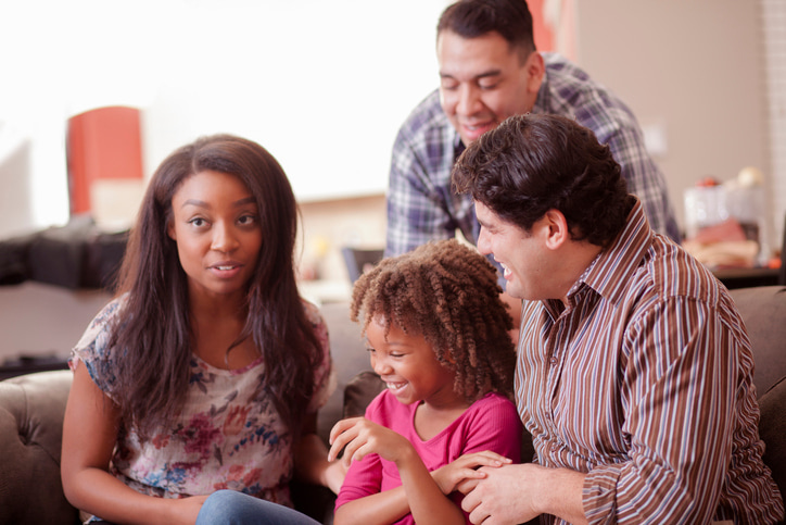 Family with two daughters and two dads smiling sitting around a couch