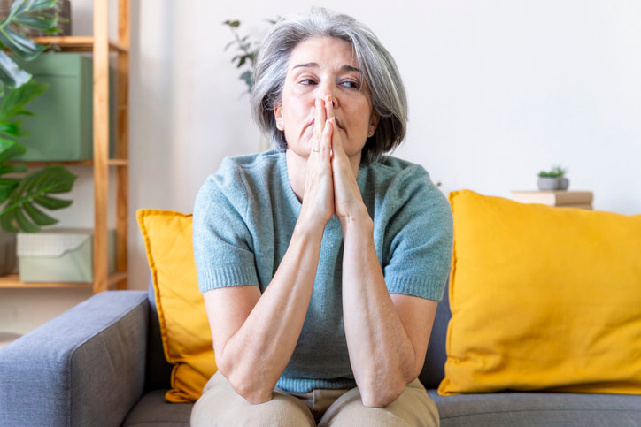 Mature adult woman feeling anxious and sad while sitting on a sofa in her living room